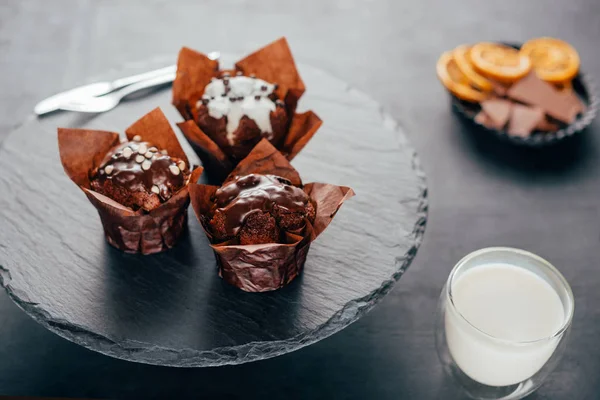 Dolci cupcake con gocce di cioccolato e bicchiere di latte su lavagna — Foto stock