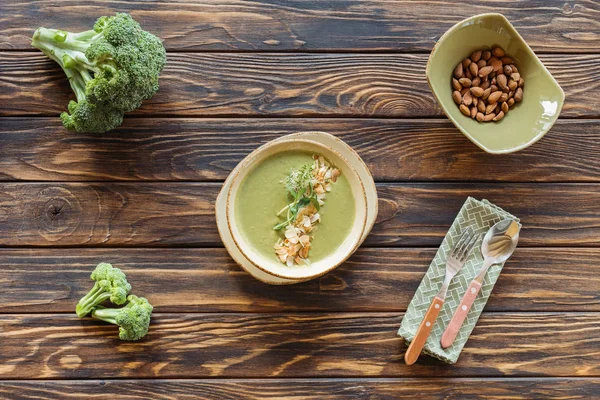 Draufsicht auf vegetarische Sahnesuppe mit Brokkoli, Rosenkohl und Mandeln in Schüssel auf Holztischplatte — Stockfoto