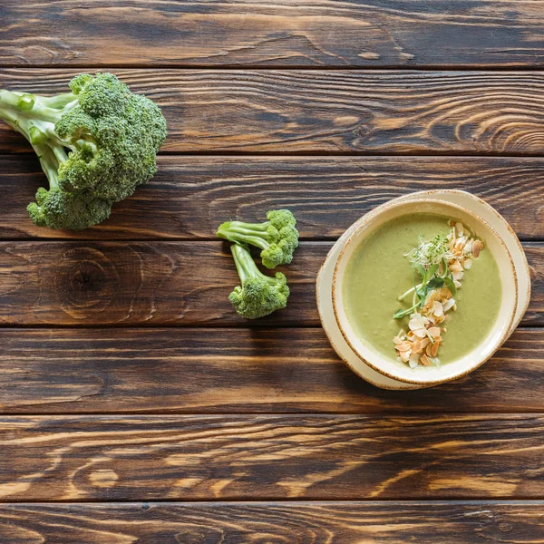 Vista superior de la sopa de crema vegetariana con brócoli, brotes y almendras en un tazón sobre una mesa de madera - foto de stock