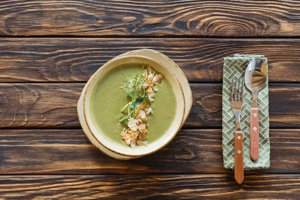 Vista superior da tigela de sopa de creme vegetariano com brócolis, brotos e amêndoas na superfície de madeira — Fotografia de Stock