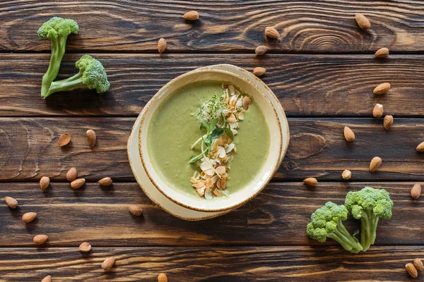 Flat lay with arranged fresh broccoli, almonds and vegetarian cream soup on wooden tabletop — Stock Photo