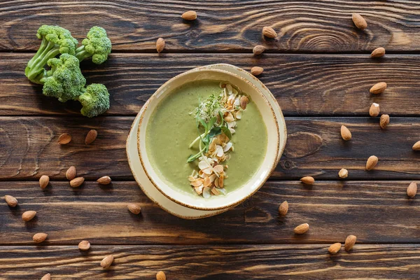 Flat lay with arranged fresh broccoli, almonds and vegetarian cream soup on wooden tabletop — Stock Photo
