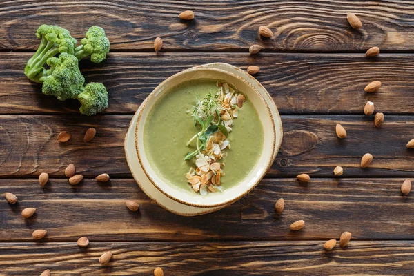 Plat avec du brocoli frais arrangé, des amandes et de la soupe à la crème végétarienne sur une table en bois — Photo de stock