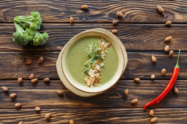 Top view of arranged vegetarian cream soup, fresh broccoli, almonds and chili peppers on wooden surface — Stock Photo