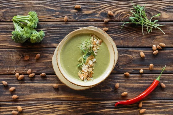 Top view of arranged vegetarian cream soup, fresh broccoli, almonds and chili peppers on wooden surface — Stock Photo