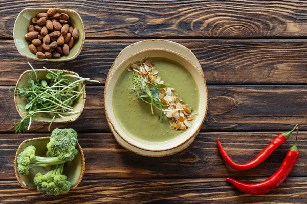 Vista superior de la sopa de crema vegetariana arreglada, brotes, almendras y brócoli fresco en cuencos en la superficie de madera - foto de stock