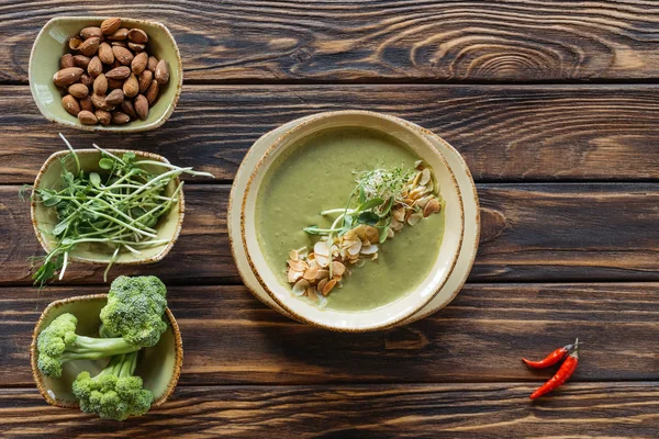 Vista dall'alto di zuppa di panna vegetariana organizzata, germogli, mandorle e broccoli freschi in ciotole su superficie di legno — Foto stock