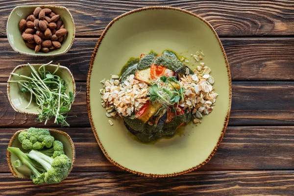 Draufsicht auf vegetarischen Salat auf Teller und frische Zutaten in Schüsseln auf hölzerner Tischplatte — Stockfoto