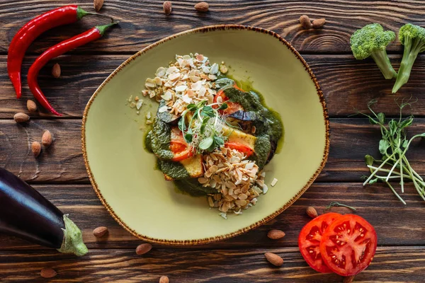 Верхний вид вегетарианского салата подается на тарелке и свежие ингредиенты расположены вокруг на деревянном столе — стоковое фото