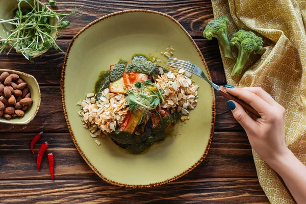 Vista parcial de la mujer con tenedor en la mesa de madera con ensalada vegetariana servida con almendras ralladas y brotes - foto de stock