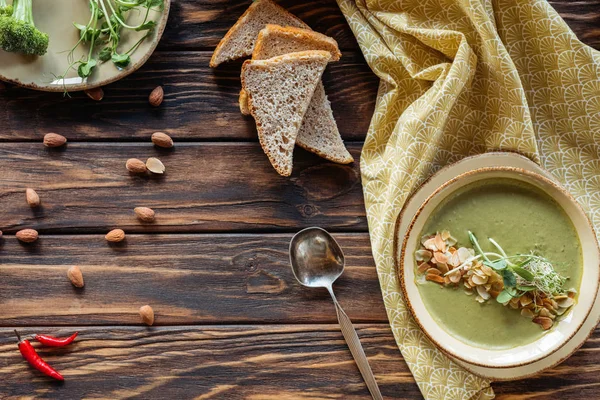 Vue du dessus de l'arrangement de la soupe à la crème végétarienne avec des germes, des morceaux de pain et des amandes sur la surface en bois — Photo de stock