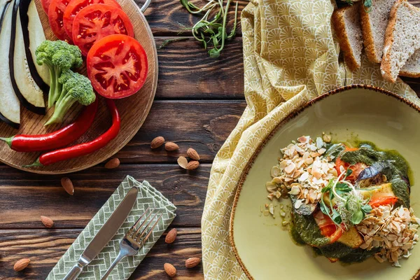 Flat lay com salada vegetariana, amêndoas, pimentas, legumes frescos e pedaços de pão em mesa de madeira — Fotografia de Stock