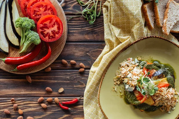 Flat lay com salada vegetariana, amêndoas, pimentas, legumes frescos e pedaços de pão em mesa de madeira — Fotografia de Stock