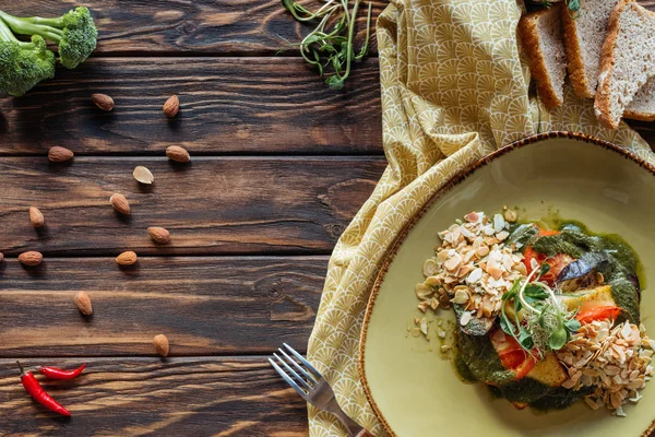 Tendido plano con ensalada vegetariana con almendras ralladas, trozos de pan, chiles y lino en la mesa de madera - foto de stock