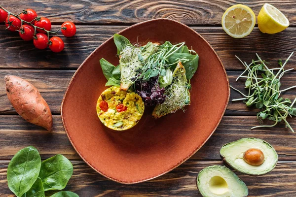 Flat lay with vegetarian salad served on plate and fresh ingredients arranged around on wooden tabletop — Stock Photo