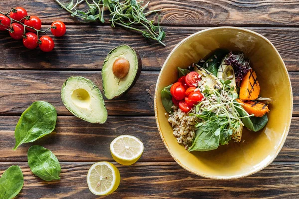 Flache Lage mit vegetarischem Salat mit gegrilltem Gemüse, Rosenkohl, Kirschtomaten in Schüssel und frischen Zutaten herum auf hölzerner Tischplatte angeordnet — Stockfoto