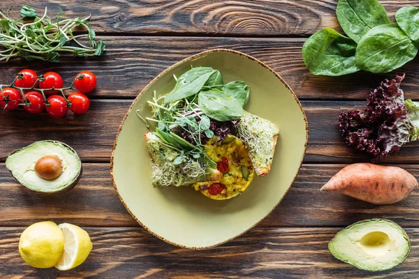 Flache Liege mit vegetarischem Salat auf Teller und frischen Zutaten auf hölzerner Tischplatte — Stockfoto