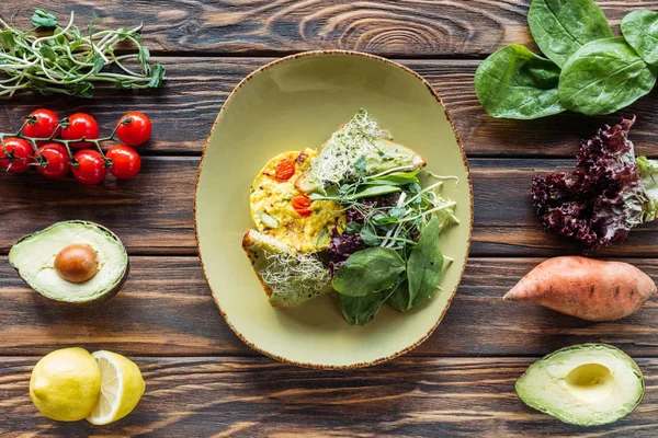 Acostado plano con ensalada vegetariana servido en el plato y los ingredientes frescos dispuestos alrededor en la mesa de madera - foto de stock