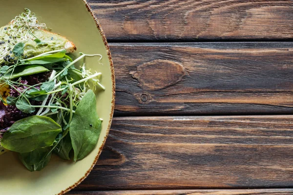 Вид зверху вегетаріанського салату зі шпинатом і паростками на тарілці на дерев'яній стільниці — стокове фото