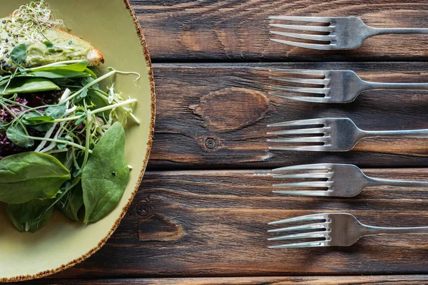 Vista superior de la ensalada vegetariana y tenedores dispuestos en la superficie de madera - foto de stock