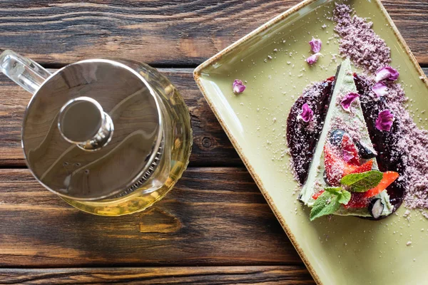 Top view of arranged vegetarian dessert with berries on plate and teapot on wooden surface — Stock Photo