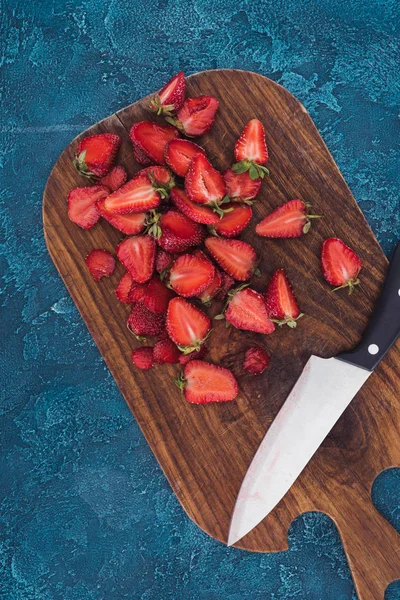 Top view of raw cut strawberries on wooden board with knife — Stock Photo