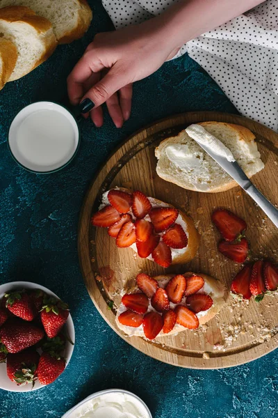 Frau kocht Brot mit Frischkäse und Erdbeeren auf Holzbrett — Stockfoto