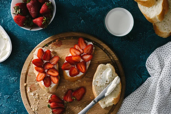 Baguette con queso crema y fresas crudas en tabla de cortar - foto de stock