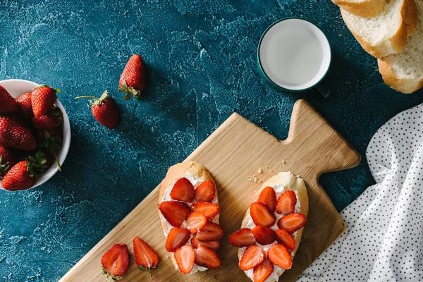 Vista superior de pão com queijo creme e morangos na mesa azul — Fotografia de Stock