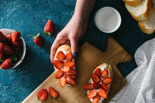 Top view of female hand holding sandwich with cream cheese and strawberries — Stock Photo