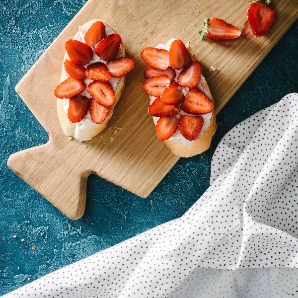 Vista dall'alto baguette con crema di formaggio e fragole crude sul tavolo con tovaglia — Foto stock