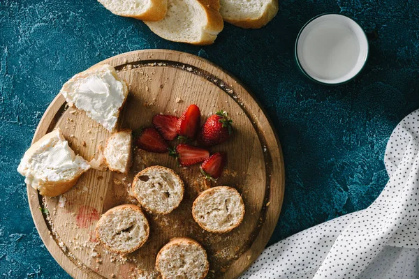 Tabla de cortar con fresas y sándwiches con queso crema en la mesa azul - foto de stock