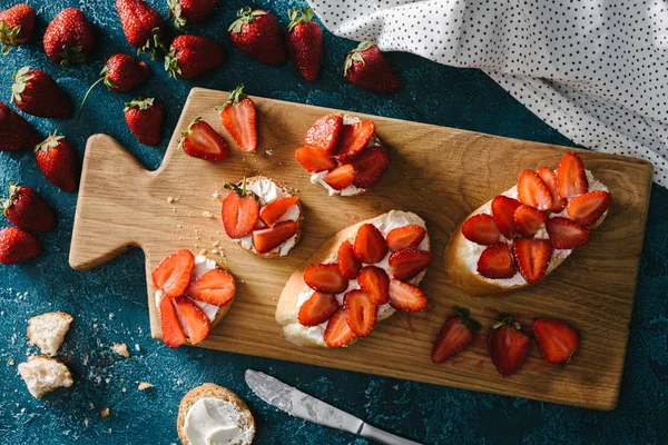 Top view of fresh strawberries by wooden board with summer sandwiches — Stock Photo