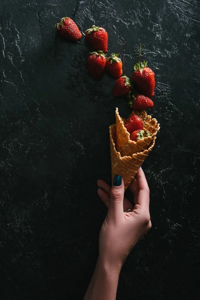 Woman holding waffle cones with raw strawberries on dark background — Stock Photo