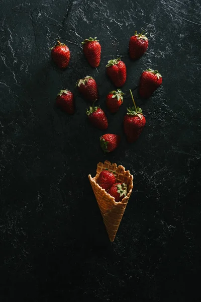 Top view of red strawberries by waffle cone on dark background — Stock Photo