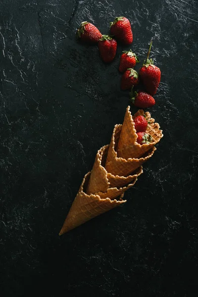 Red strawberries by stacked waffle cones on dark background — Stock Photo