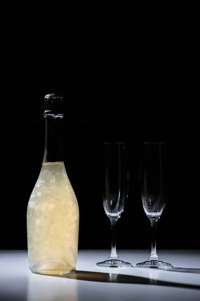 Close up view of bottle of champagne and empty glasses on black background — Stock Photo