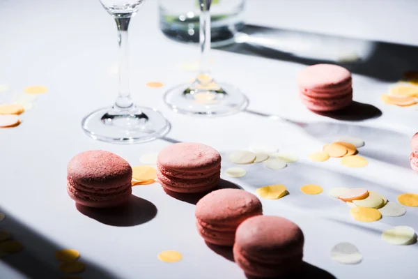 Vista de cerca de macarrones dulces arreglados y cristalería en la mesa - foto de stock