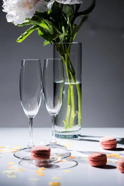 Nahaufnahme leerer Gläser, süßer Macarons und Blumenstrauß in der Vase vor grauem Hintergrund — Stockfoto