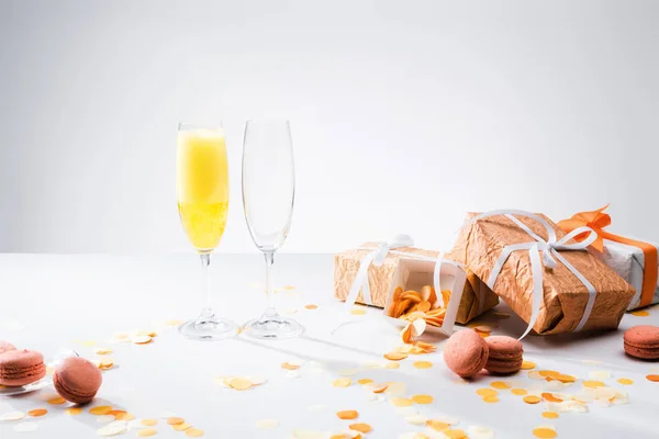 Nahaufnahme von Gläsern mit gelbem Champagner, Macarons und arrangierten Geschenken auf grauem Hintergrund — Stockfoto