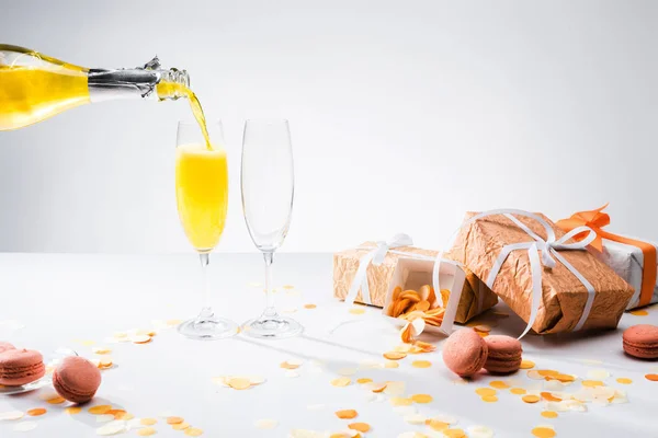 Vue rapprochée de verser du champagne jaune dans le processus de verrerie et des cadeaux arrangés sur fond gris — Photo de stock