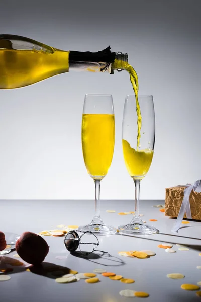 Close up view of pouring yellow champagne into glassware process and arranged gifts on grey backdrop — Stock Photo