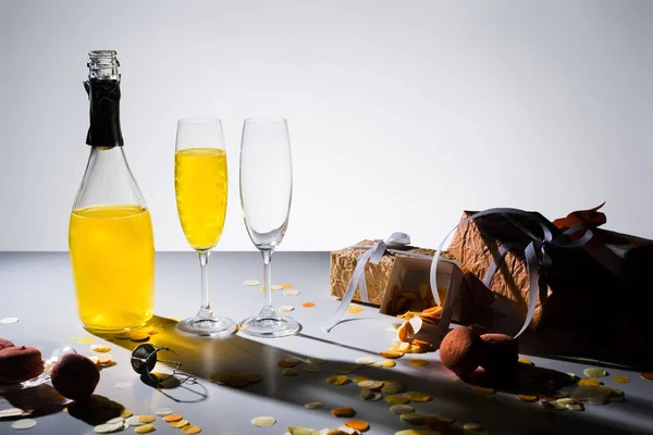 Close up view of glassware with yellow champagne, macarons and arranged gifts on grey backdrop — Stock Photo