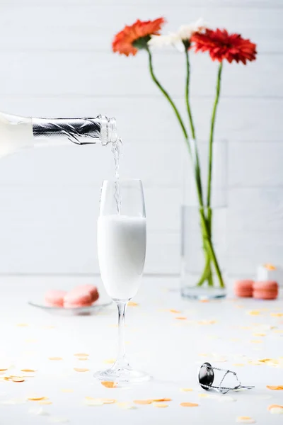Messa a fuoco selettiva di versare champagne nel processo di vetro, maccheroni e mazzo di fiori su sfondo grigio — Foto stock