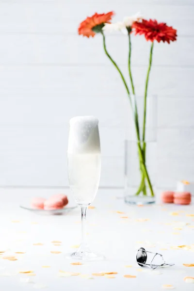 Selective focus of glass full of champagne and macarons on grey background — Stock Photo