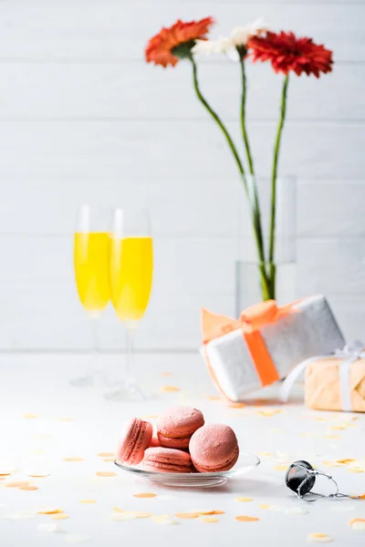 Foyer sélectif de macarons doux, fleurs dans un vase, cadeaux et verres de champagne jaune sur fond gris — Photo de stock