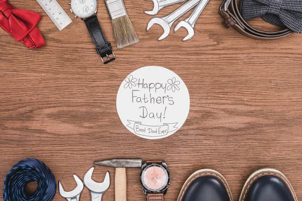 Vista superior de la tarjeta de felicitación del día del feliz padre rodeada de atribución de padres en la superficie de madera - foto de stock