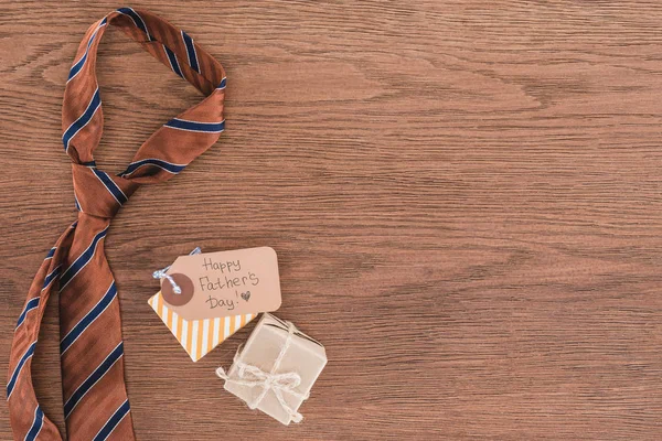 Vista superior de la corbata con regalos y felicitación feliz día de los padres en la mesa de madera - foto de stock