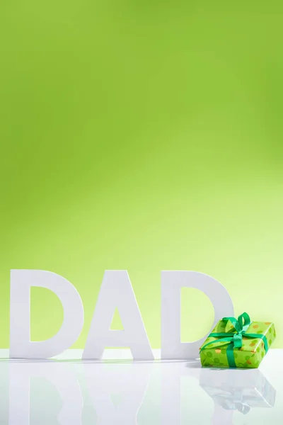 Green gift box in front of dad inscription made of white letters on green, Happy fathers day concept — Stock Photo