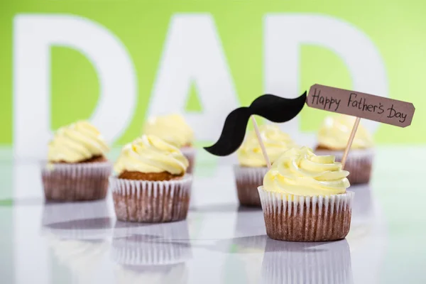 Creamy cupcakes with mustache sign and Happy fathers day inscription in front of dad inscription made of white letters on green — Stock Photo